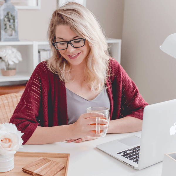 Lächelnde Frau vor Ihrer Arbeit am Macbook genießt ihren morgendlichen Tee
